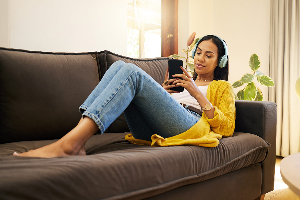Woman on couch looking at phone with headphones on